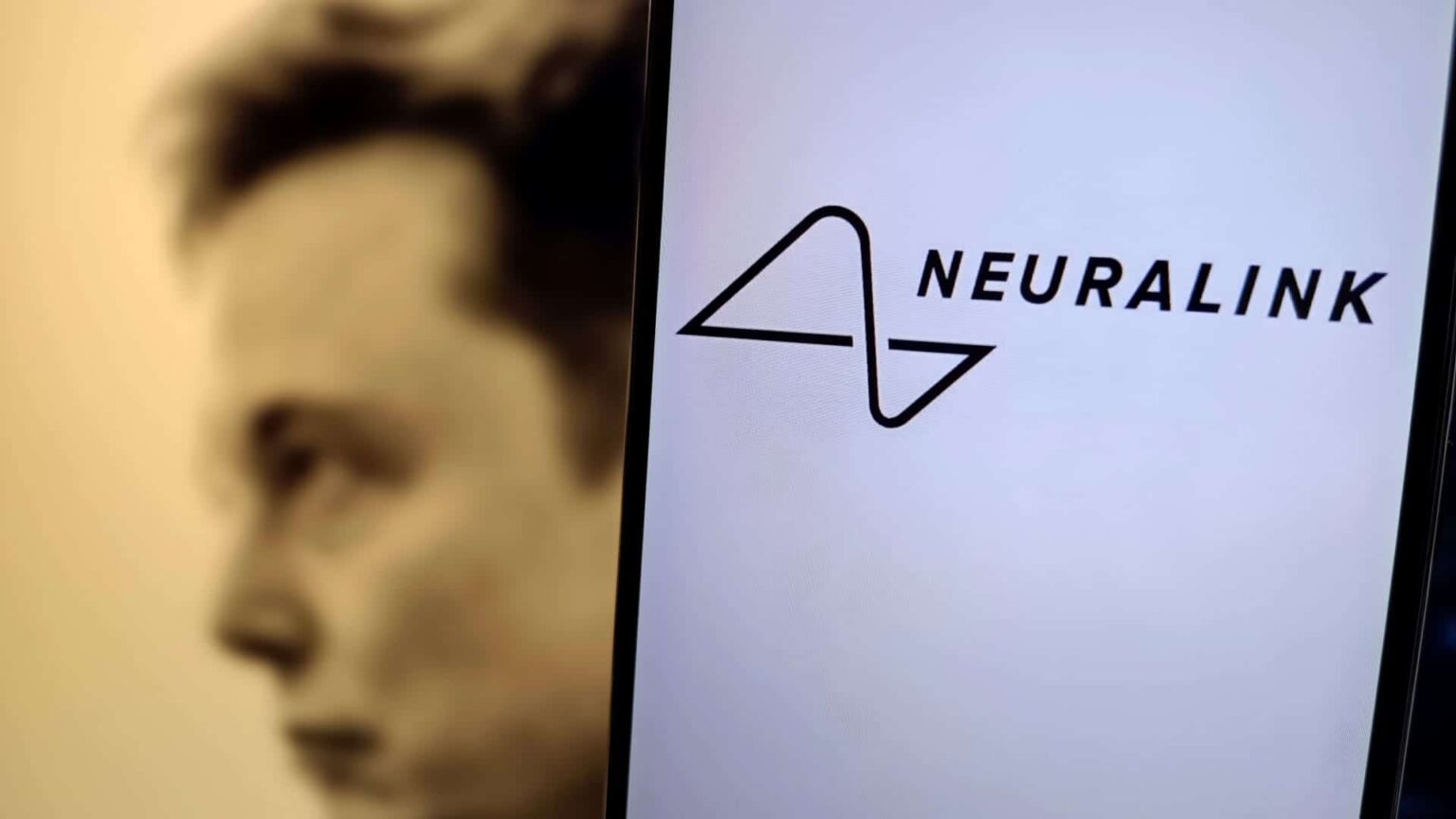 Logotipo da Neuralink exibido na tela de um celular, com o rosto desfocado de um homem ao lado