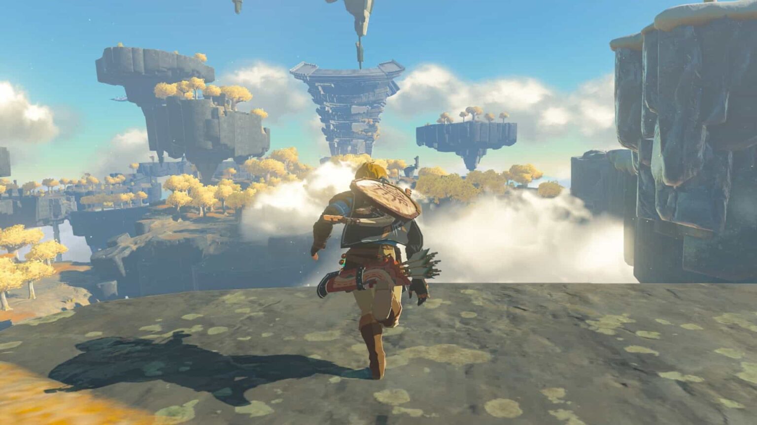 Captura de tela de Zelda: Tears of the Kingdom mostrando Link correndo de costas sobre uma plataforma de pedra, com ilhas flutuantes e nuvens ao fundo