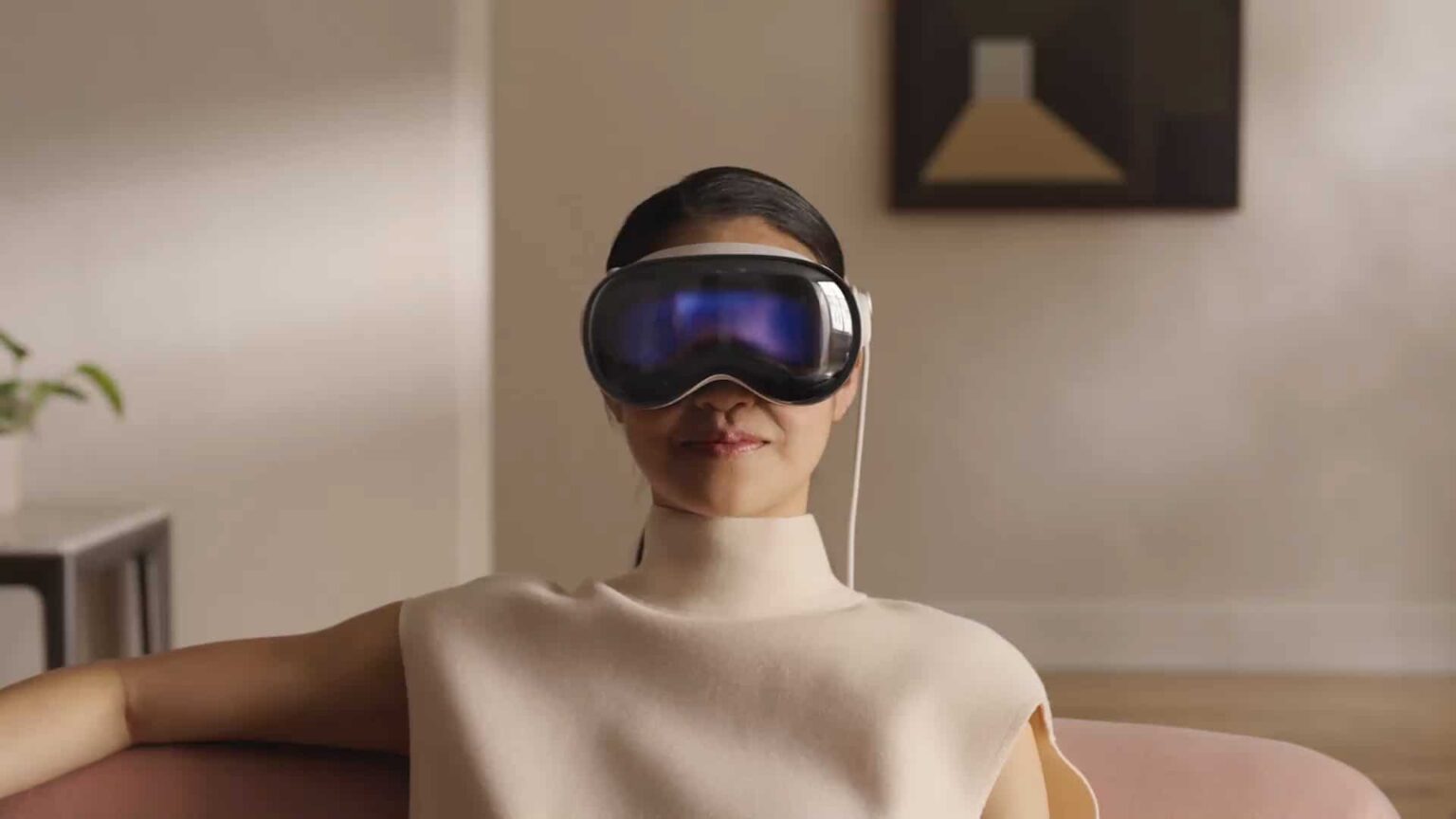 Mulher sentada em um sofá usando um headset de realidade virtual branco com lente espelhada azulada, em ambiente de sala clara