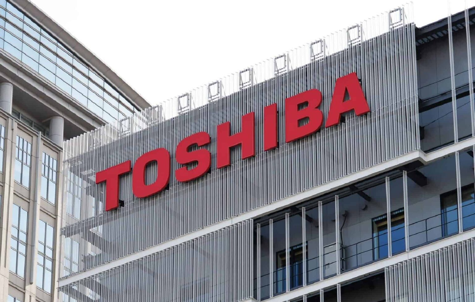 Fachada de prédio moderno com letreiro vermelho da marca Toshiba sobre painéis metálicos verticais e janelas de vidro