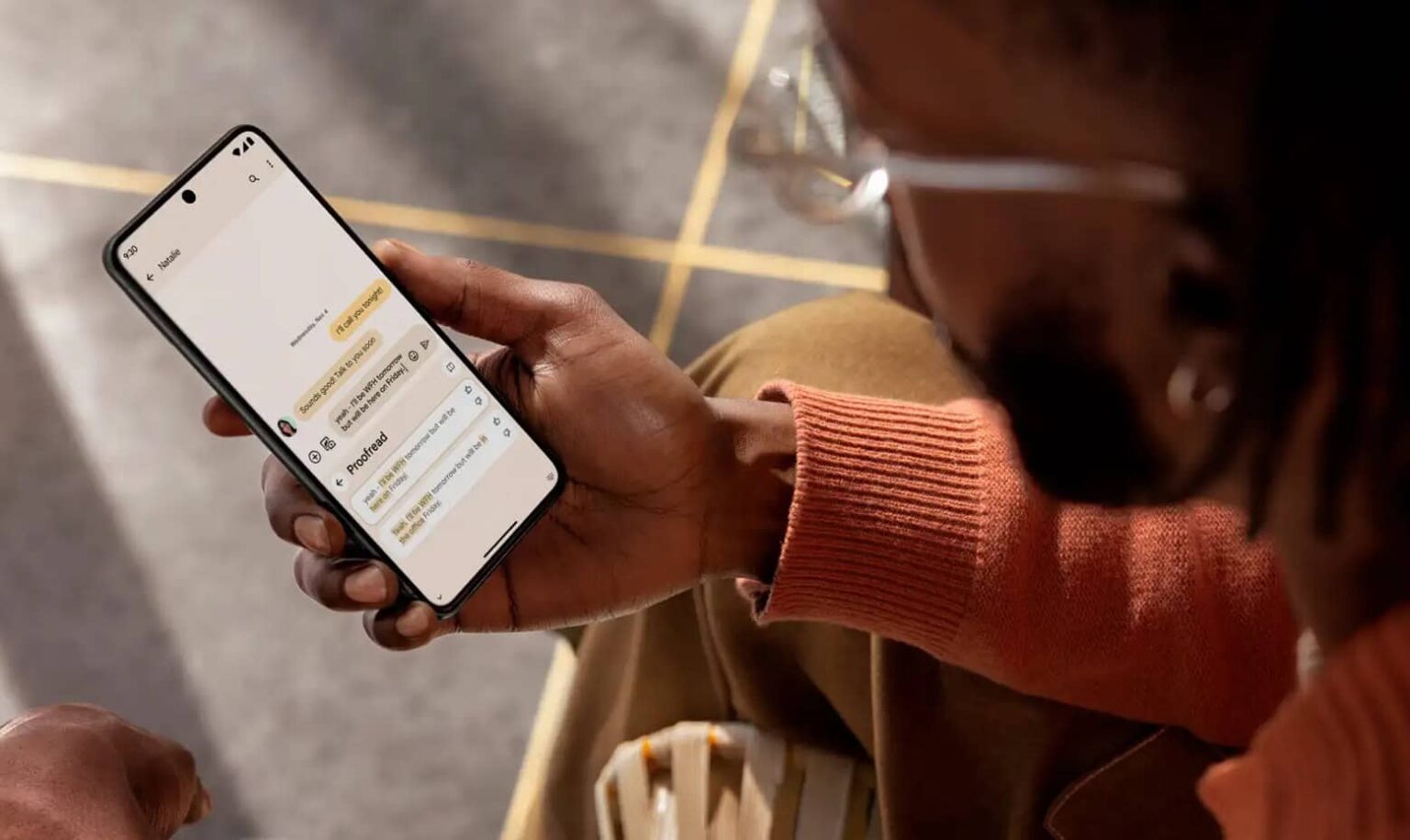 Pessoa de óculos segurando smartphone com tela de aplicativo de mensagens aberta, em uma rua ensolarada