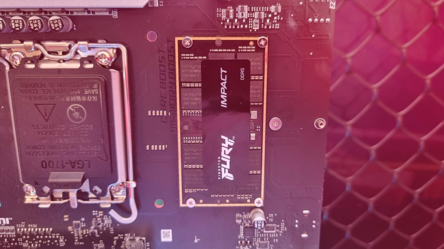 Placa-mãe com soquete LGA 1700 e, ao lado, módulo de memória CAMM2 Kingston Fury Impact DDR5 instalado sobre a placa, sob luz avermelhada