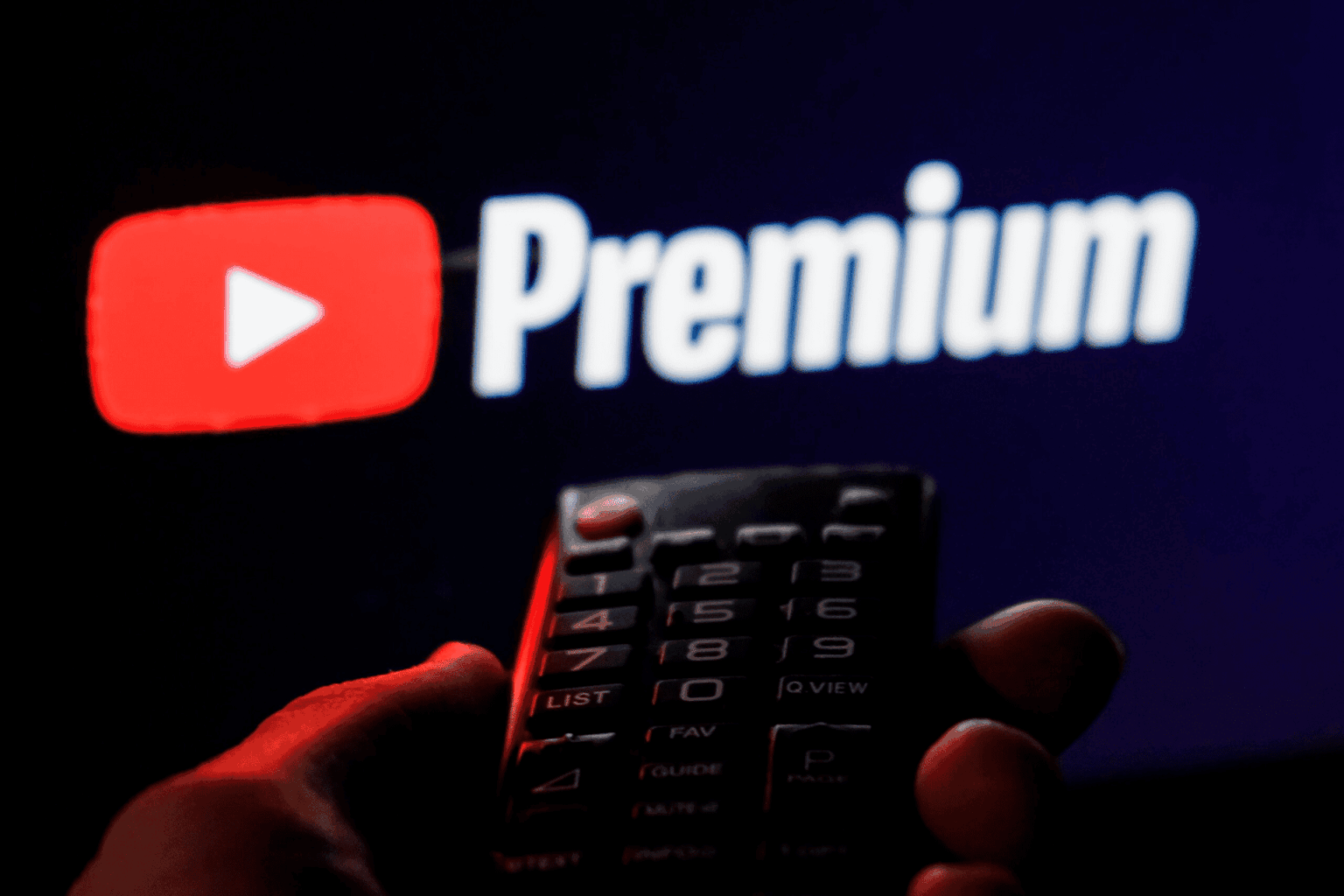 Mão segurando um controle remoto de TV em frente à logo do YouTube Premium exibida na tela escura