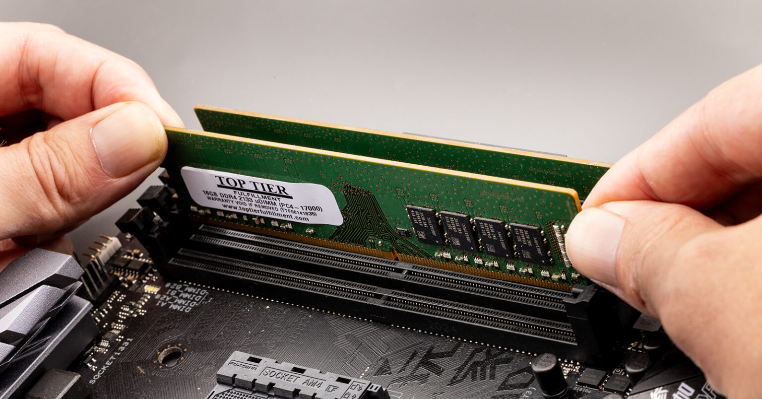 Mãos encaixando um pente de memória RAM DDR4 com etiqueta Top Tier em um slot de placa-mãe preta com detalhes em cinza