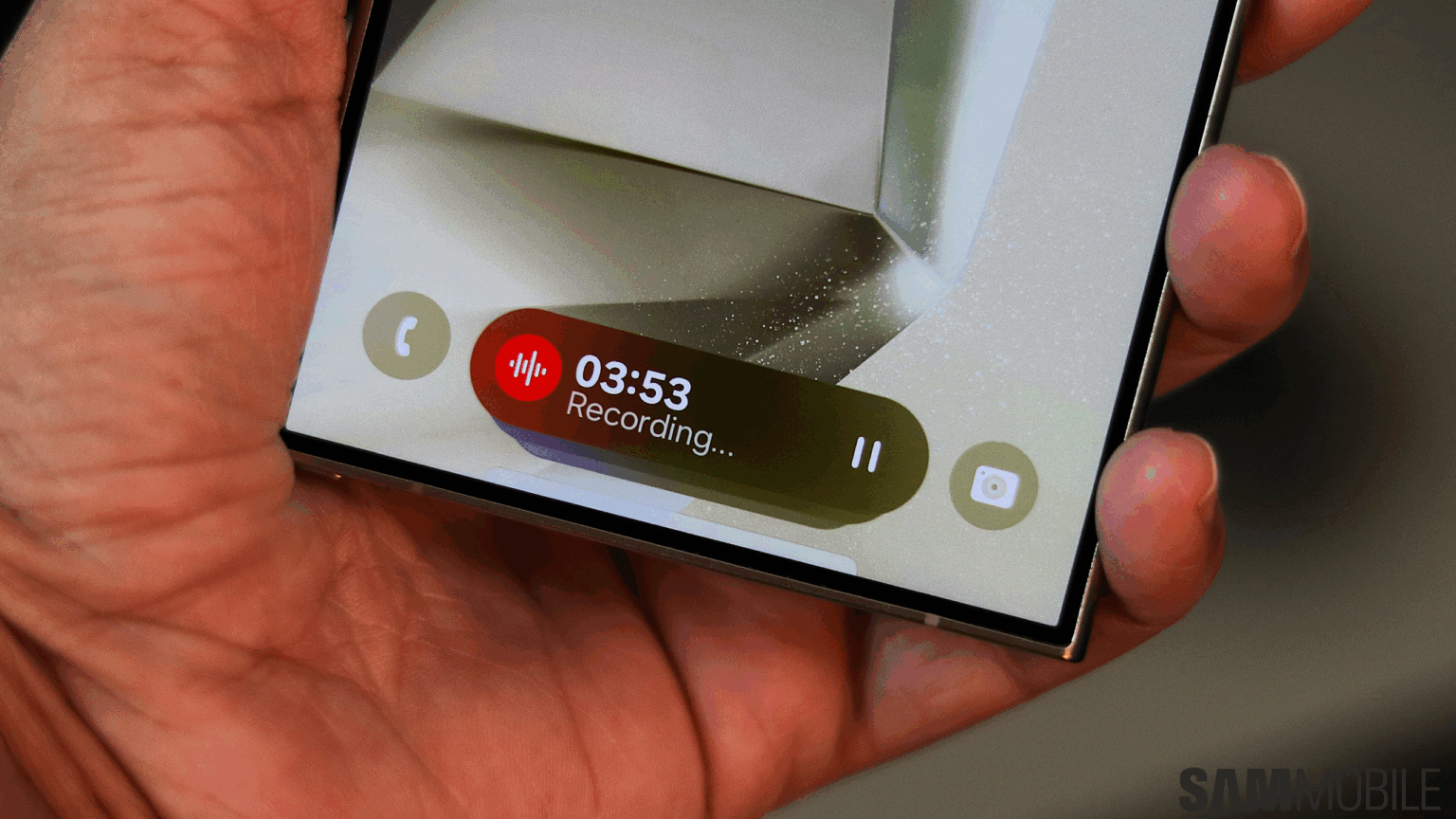 Mão segurando celular Samsung com gravação de voz ativa na tela, exibindo o cronômetro 03:53 e o texto "Recording..." em notificação flutuante