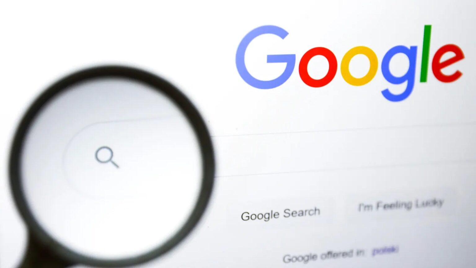 Lupa sobre a tela inicial do Google, com a caixa de busca em destaque e os botões "Google Search" e "I'm Feeling Lucky