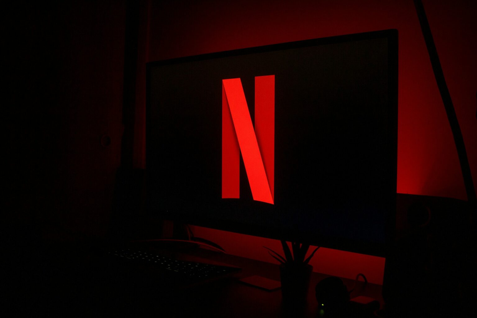 Monitor de computador em ambiente escuro exibindo o logotipo vermelho da Netflix sobre fundo preto, com iluminação vermelha ao redor