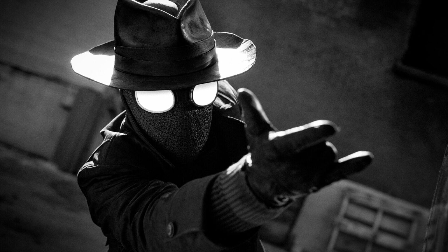 Personagem de chapéu fedora e máscara com olhos brilhantes estendendo a mão enluvada em direção à câmera, em preto e branco, num cenário urbano noir