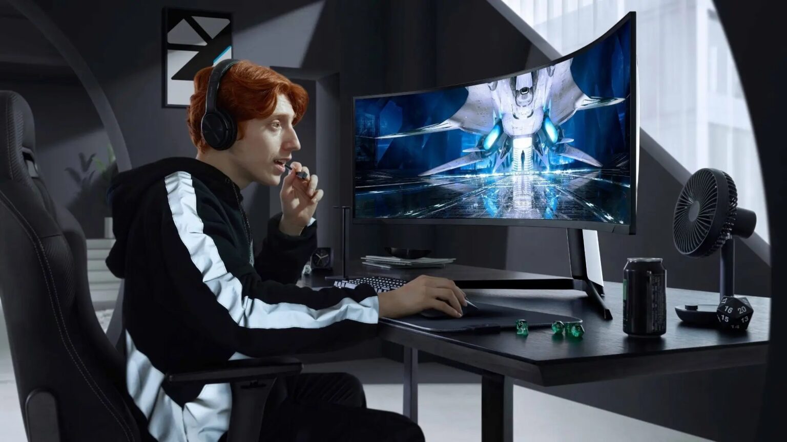 Homem de fones de ouvido jogando em monitor curvo ultrawide sobre mesa escura, com ventilador e latas de energético ao lado