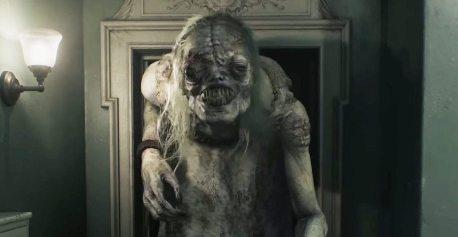 Criatura monstruosa e pálida com dentes expostos e cabelos desgrenhados, em corredor de casa antiga iluminado por arandela, cena do jogo Resident Evil