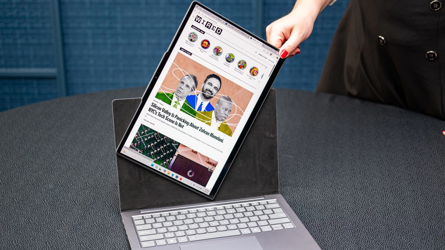 Notebook com tela destacável em formato tablet, mostrando o site da revista Wired sobre o Vale do Silício, sobre uma mesa escura de feira de tecnologia