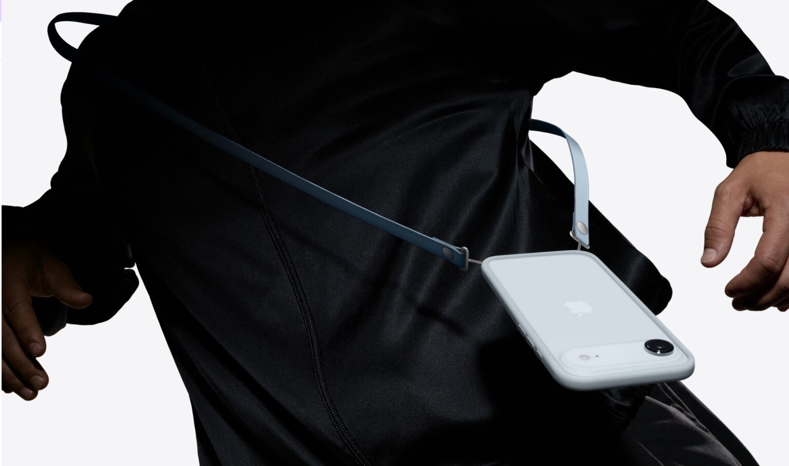 Pessoa de roupa preta usando iPhone 17 branco preso a uma alça crossbody azul-escura na cintura, com a parte traseira do aparelho à vista