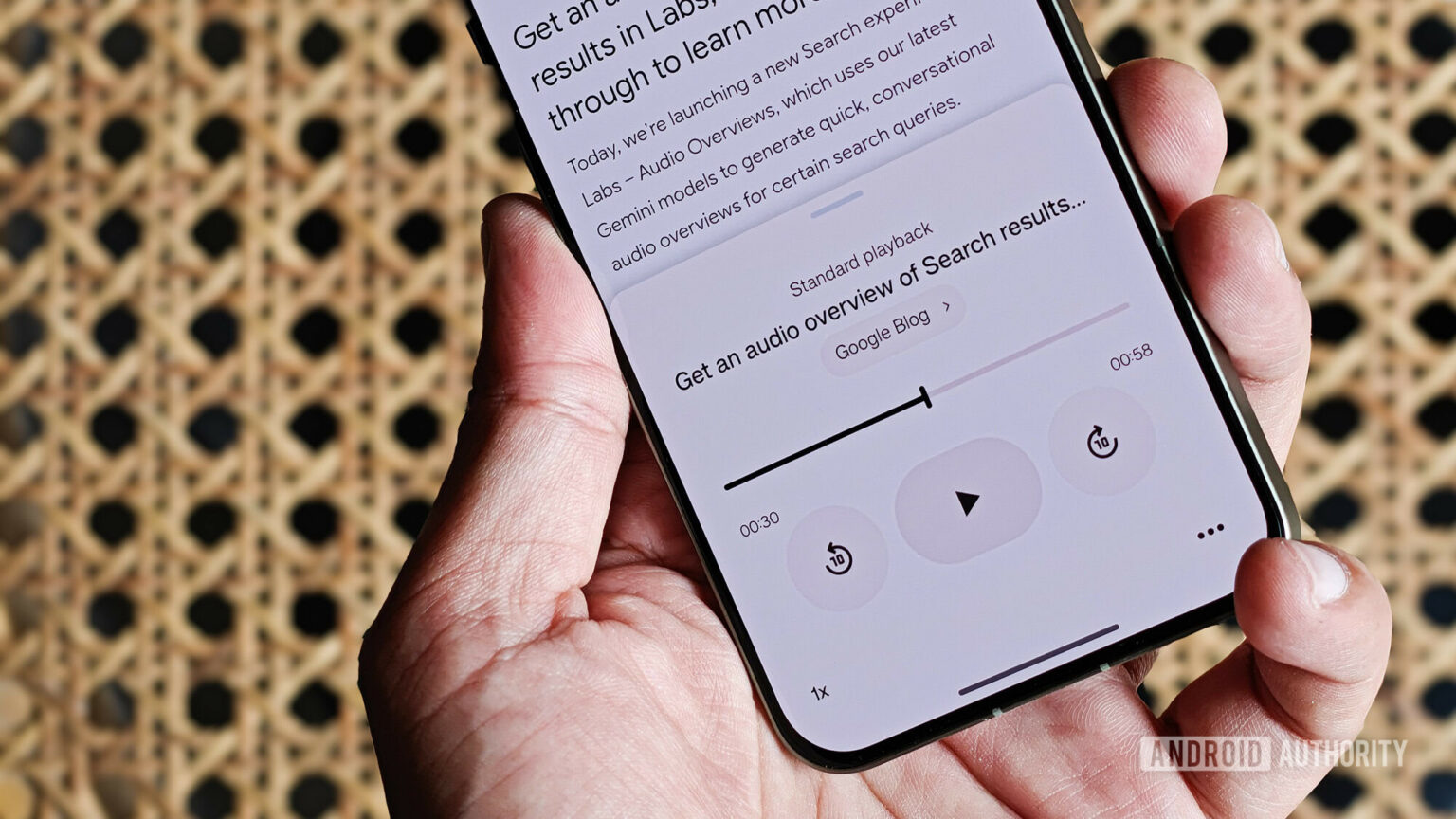 Mão segurando smartphone exibindo player de áudio com resumo em voz gerada por IA de uma página do Google Blog, com controles de reprodução e tempo de 00:58