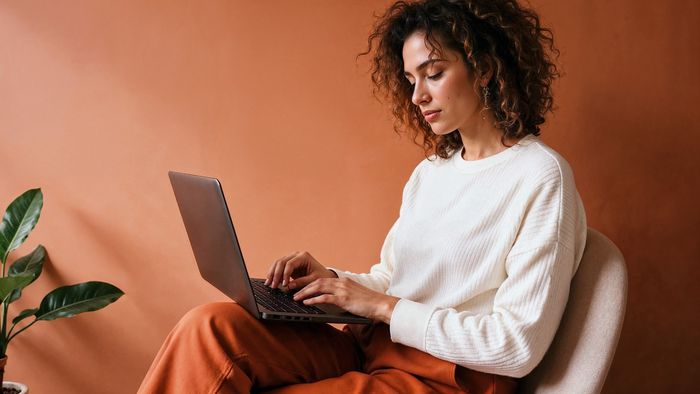 Parece que o jogo virou: Mulheres agora usam mais o ChatGPT que os homens, revela estudo 1 Mulher adulta usando laptop em ambiente com iluminação quente e parede laranja terroso
