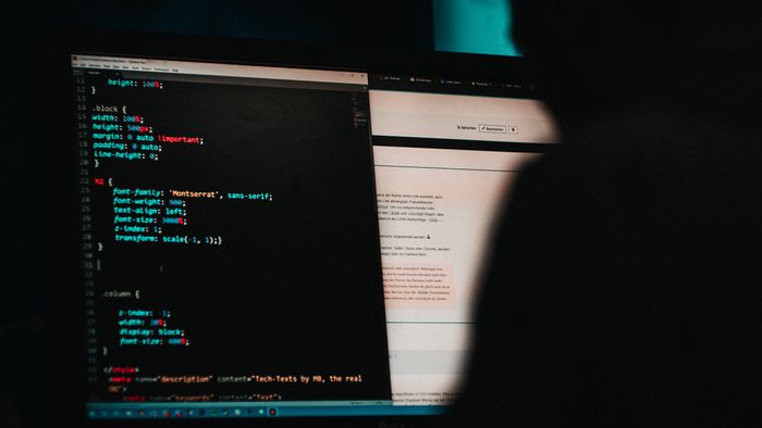 Raven Stealer: o malware que rouba suas senhas do Chrome e Edge sem deixar rastro 1 Pessoa programando em computador com código-fonte exibido em tela escura