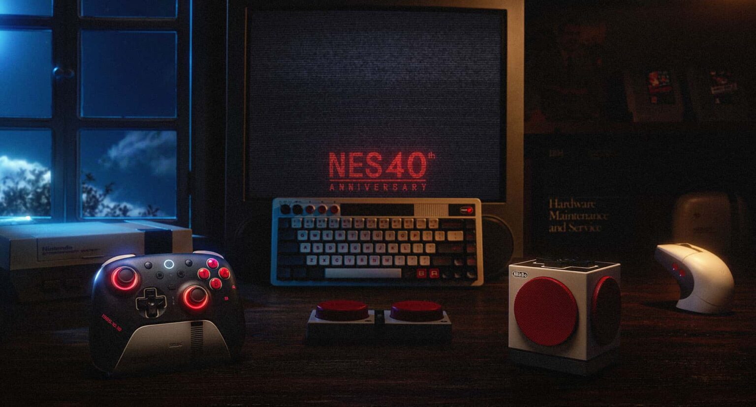 Mesa com controle 8BitDo de estilo NES, teclado retrô, botões vermelhos e monitor exibindo "NES 40th Anniversary" em cena noturna