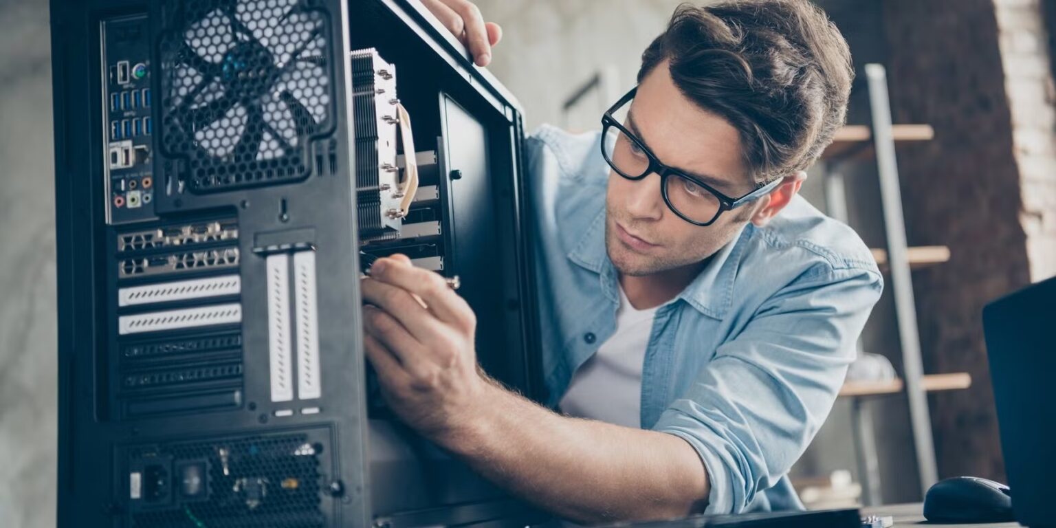 Homem de óculos limpando o interior de um gabinete de computador com cooler e placas de expansão à mostra