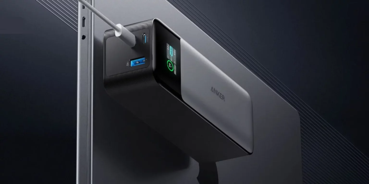 Power bank Anker preto com tela digital e portas USB-C e USB-A, conectado por cabo USB-C a um notebook de tela cinza