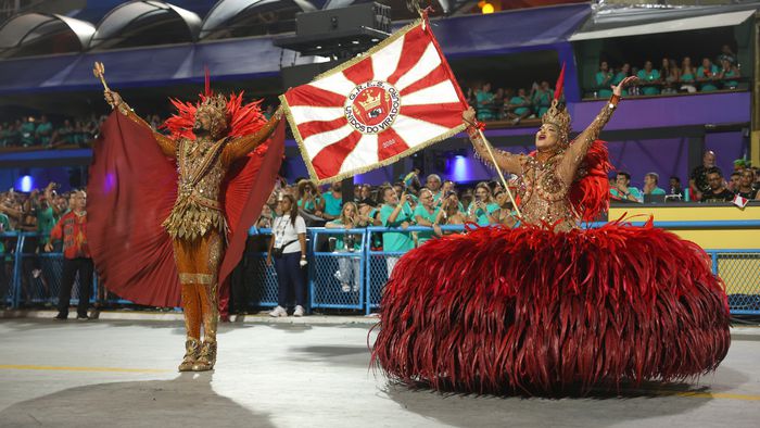 Unidos do Viradouro usa IA para trazer de volta a voz de Dominguinhos do Estácio 1 Apresentação de escola de samba Unidos do Viradouro com dançarinos em figurinos dourados elaborados e penas vermelhas em estádio de Carnaval