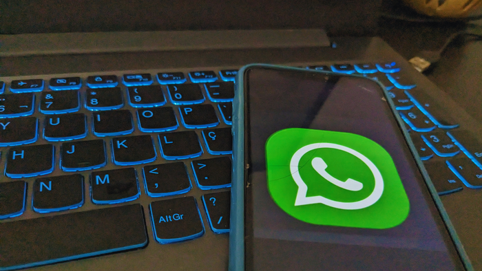 Bug no WhatsApp Beta faz mensagens sumirem após atualização 1 Smartphone com capa azul apoiado diagonalmente sobre teclado de notebook, com o ícone do WhatsApp visível na tela do aparelho