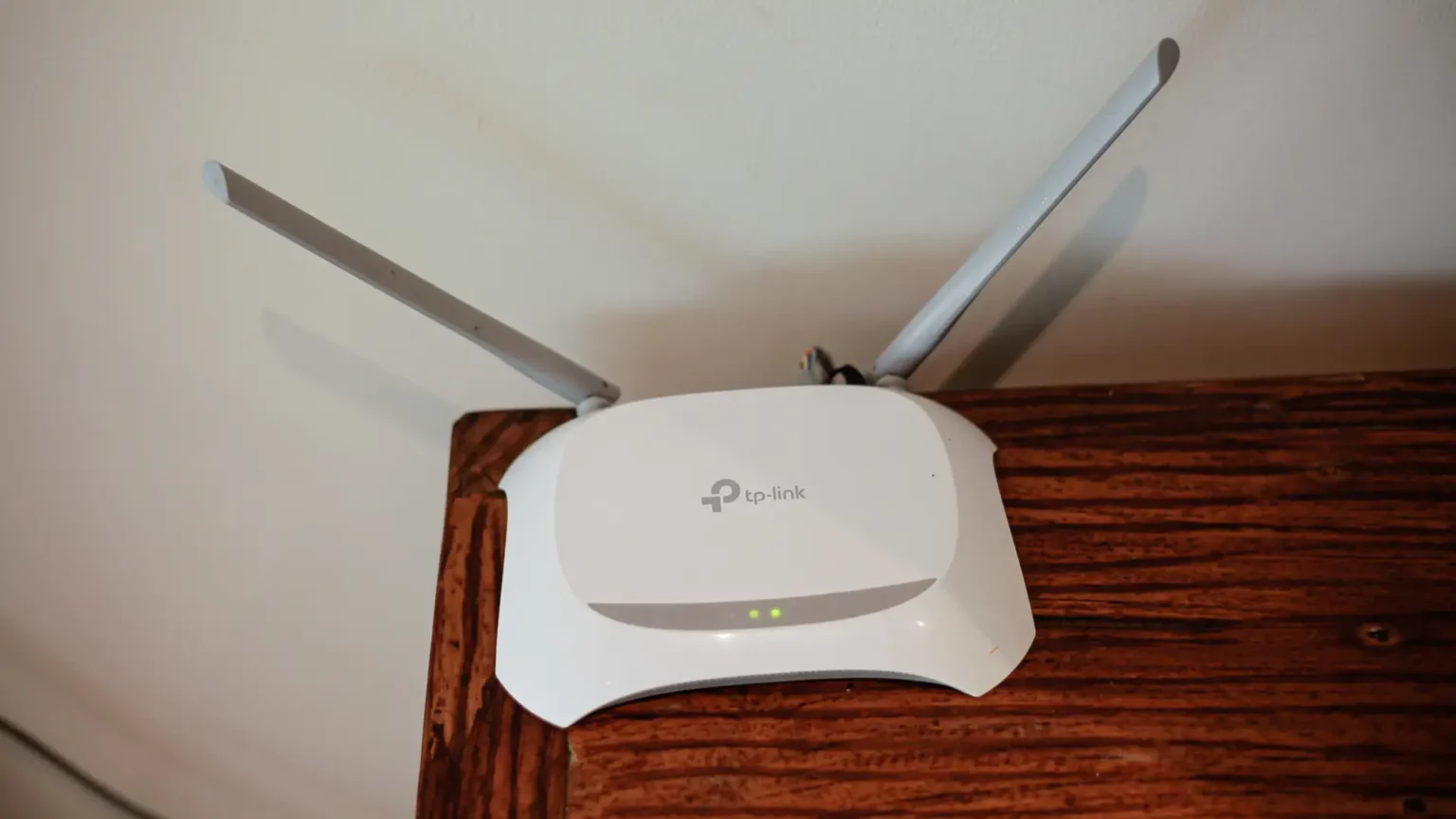 Roteador TP-Link branco com duas antenas externas, apoiado sobre uma mesa de madeira e fixado próximo a uma parede clara