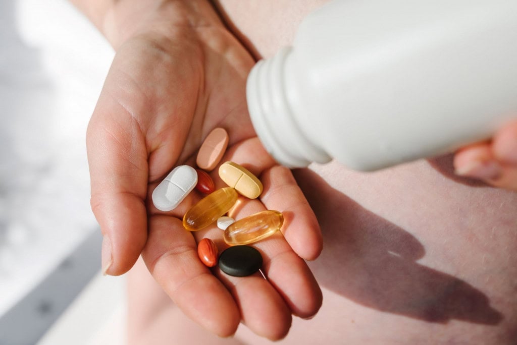 Robôs estão acelerando a criação de antibióticos antibióticos em tempo recorde 1 Mão segurando várias pílulas e cápsulas coloridas e translúcidas, com garrafa branca derramando mais pílulas na palma
