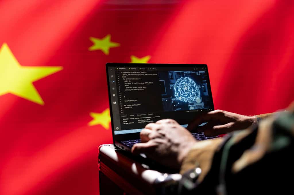China estabelece novas regras para IAs que simulam emoções humanas 2 Mãos sobre teclado de laptop com tela mostrando código e ilustração azul de rede neural, fundo com a bandeira da China desfocada