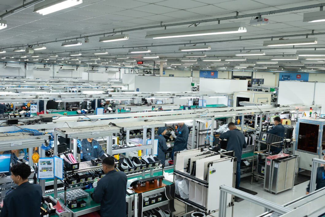 Fábrica moderna de montagem de hardware eletrônico com trabalhadores em estações de produção, cabos e componentes em linhas de montagem