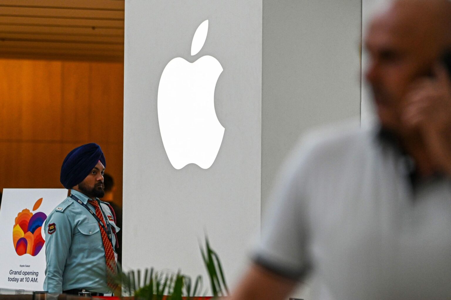 Segurança de turbante azul ao lado de cartaz de inauguração da loja Apple na Índia, com o logo da maçã iluminado ao fundo