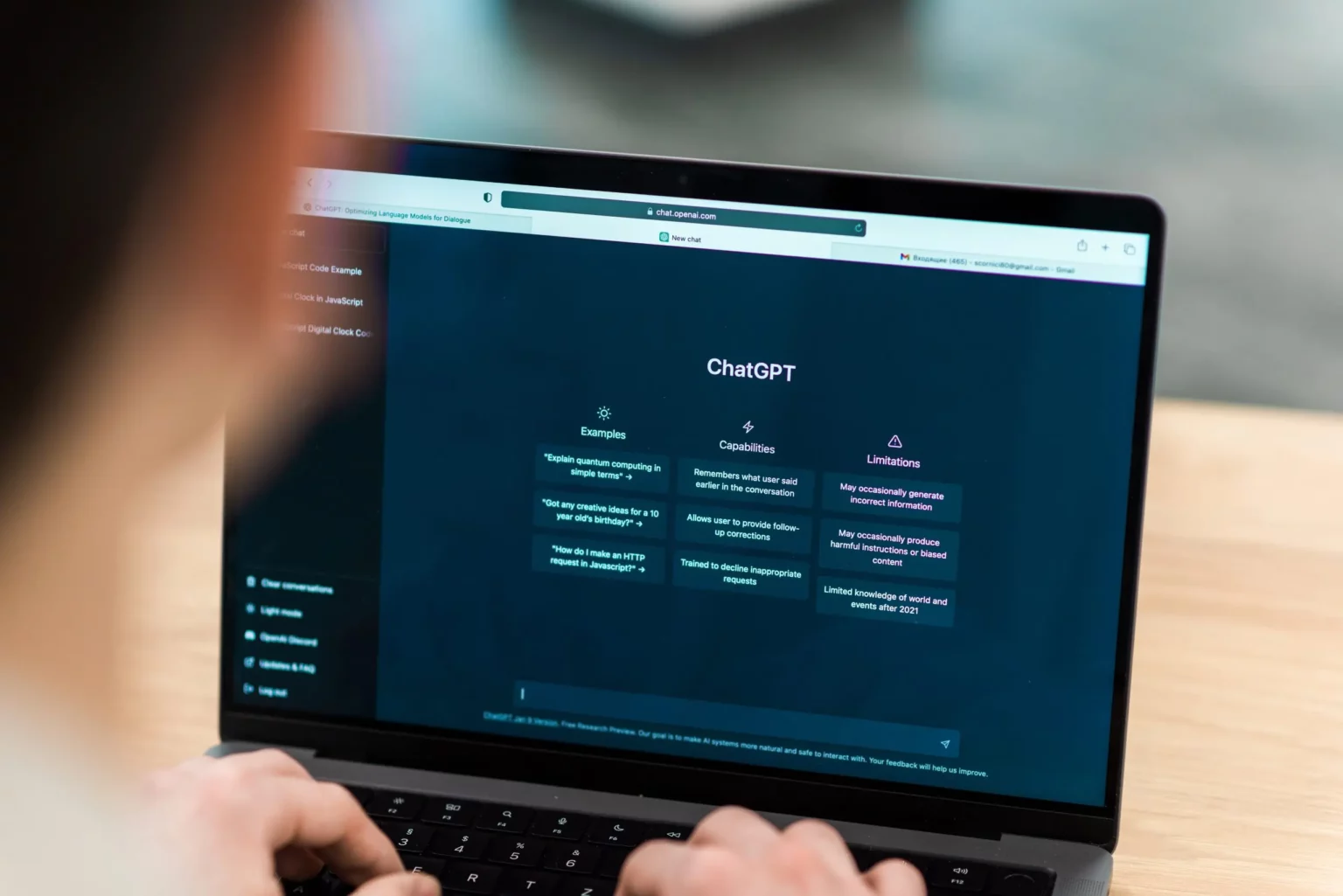 Pessoa digitando em notebook com a página inicial do ChatGPT aberta, com exemplos, recursos e limitações listados na tela escura
