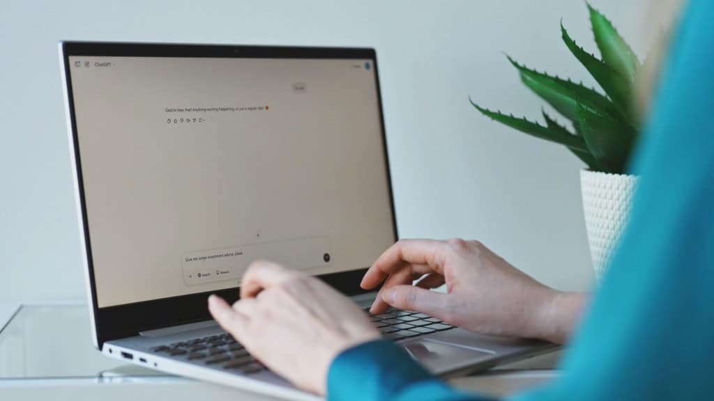 Notebook aberto com conversa em chat de inteligência artificial na tela e mãos digitando