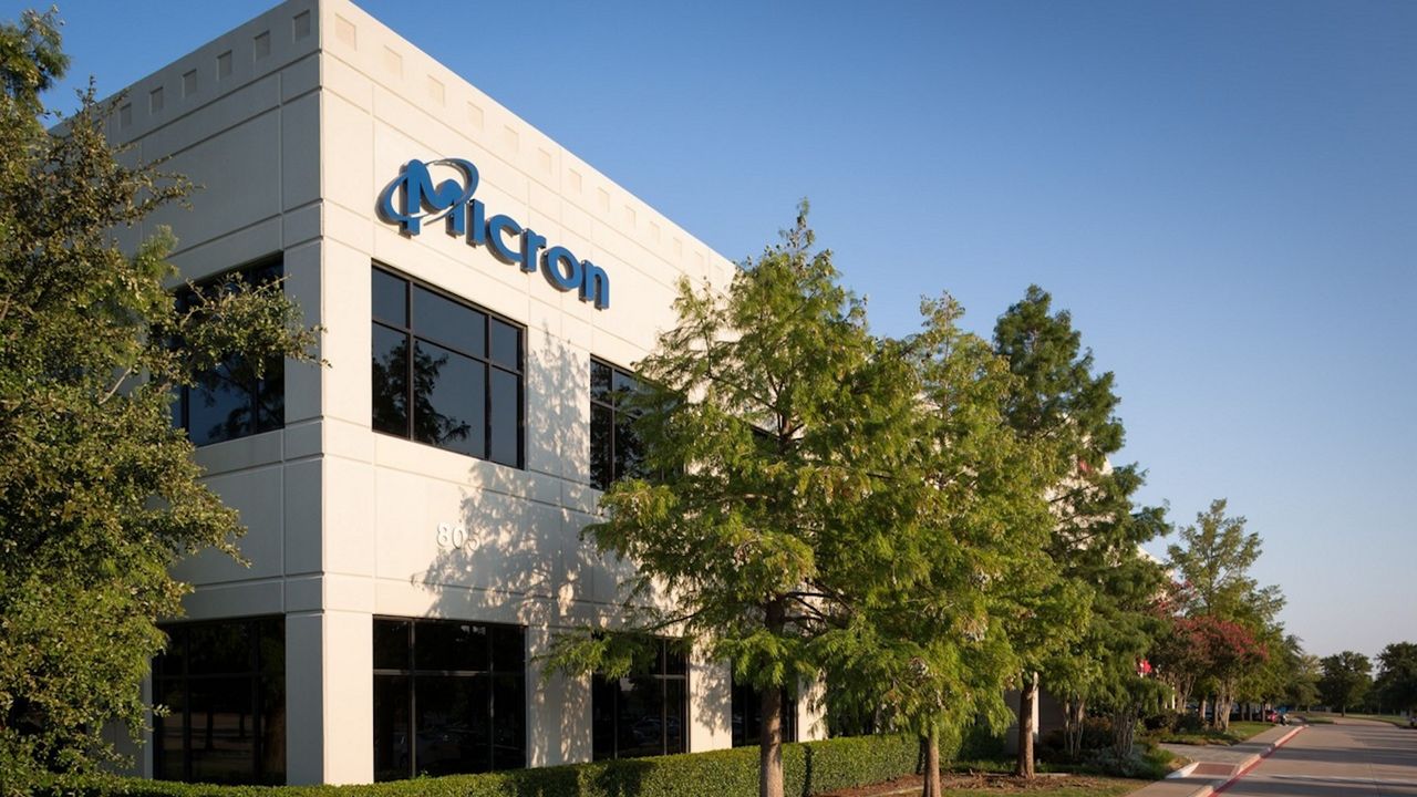 Prédio corporativo moderno da Micron com fachada clara e logo azul, ambiente de parque tecnológico em dia ensolarado