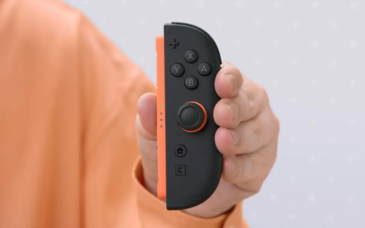 Mão segurando Joy-Con preto do Nintendo Switch 2 com faixa laranja e botões X Y A B