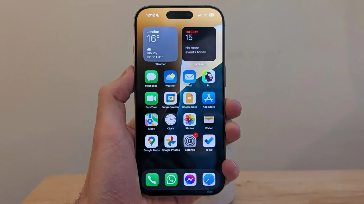 Mão segurando um iPhone exibindo a tela inicial com widgets de clima e calendário, além de apps como Mensagens, FaceTime, Google Agenda, Mapas e Ajustes