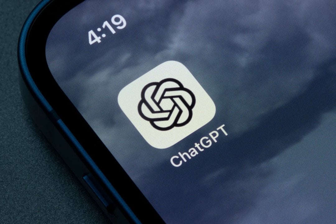 Tela de smartphone mostrando o ícone do aplicativo ChatGPT, com o nome abaixo do ícone, sobre um fundo de céu nublado