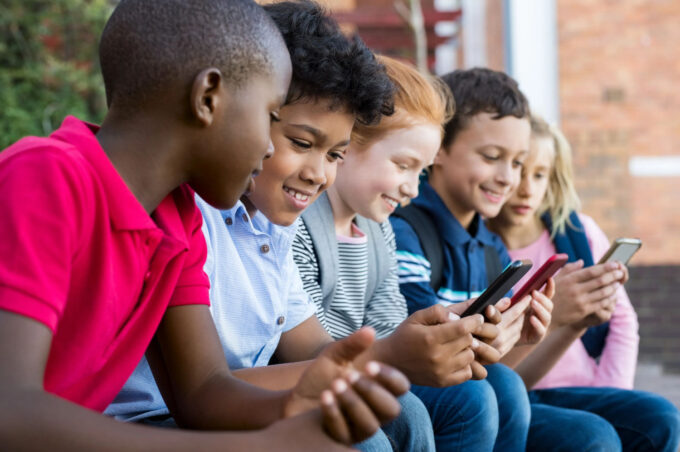Grupo de crianças diversas em área externa segurando smartphones e usando redes sociais