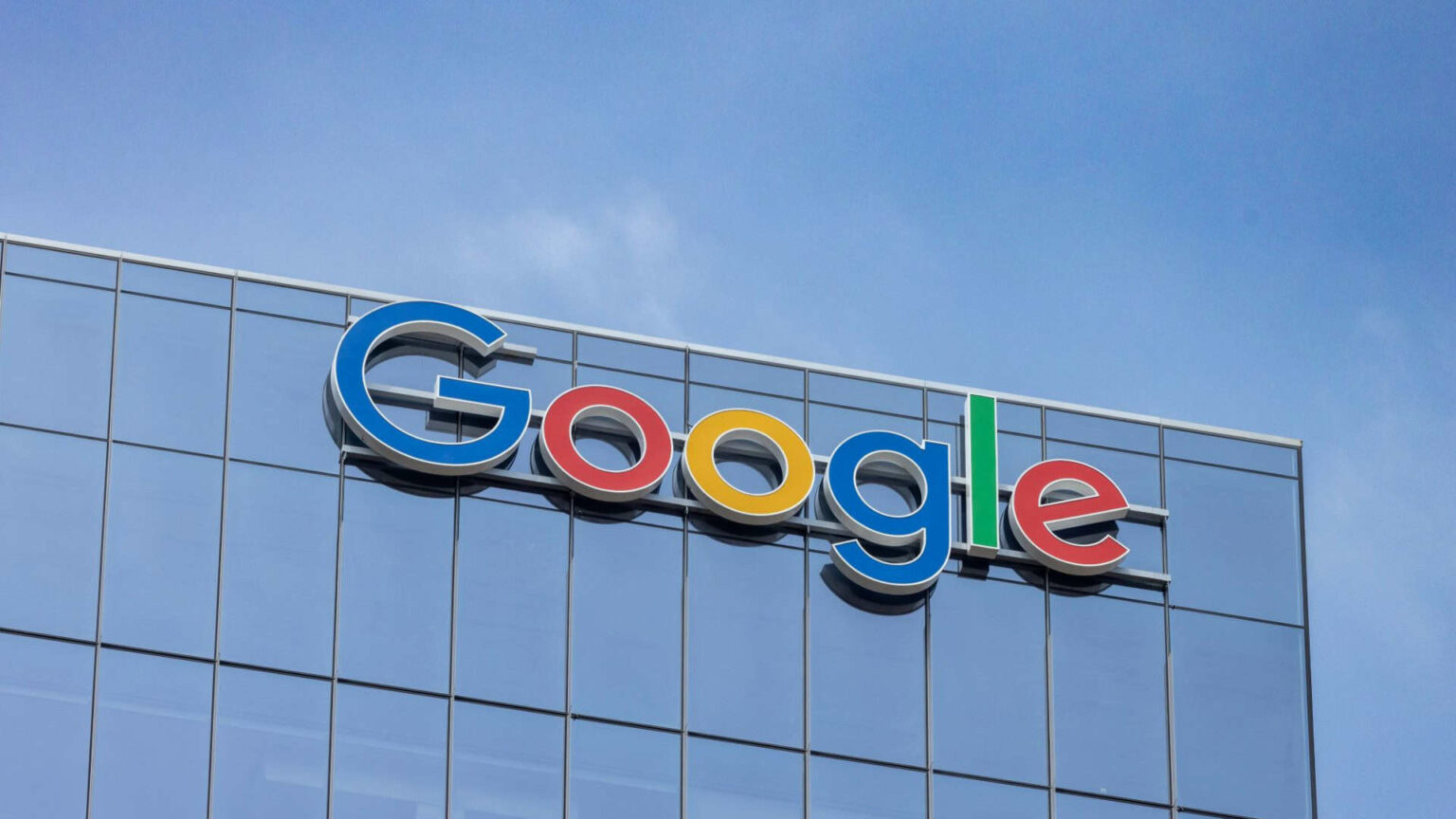 Letreiro em letras 3D coloridas do Google no topo de um prédio de vidro espelhado, sob céu azul