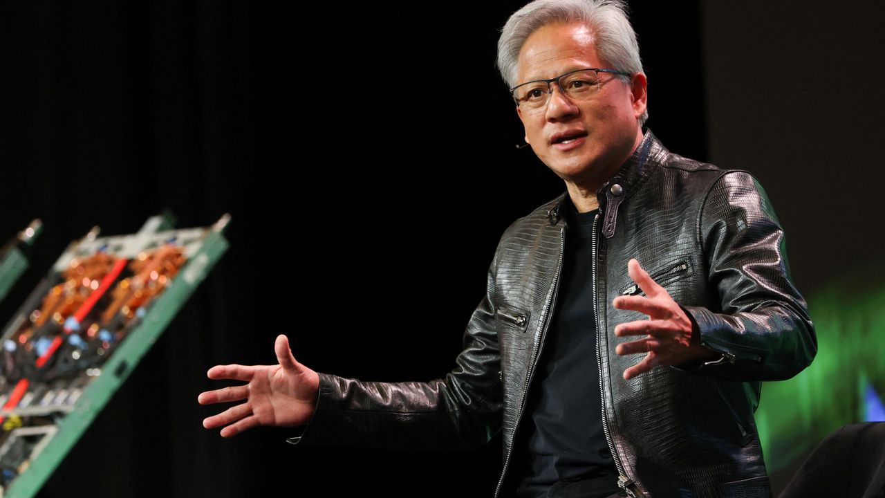 Jensen Huang apresentando em evento de tecnologia com jaqueta preta e fundo escuro com luz verde e painel técnico ao lado