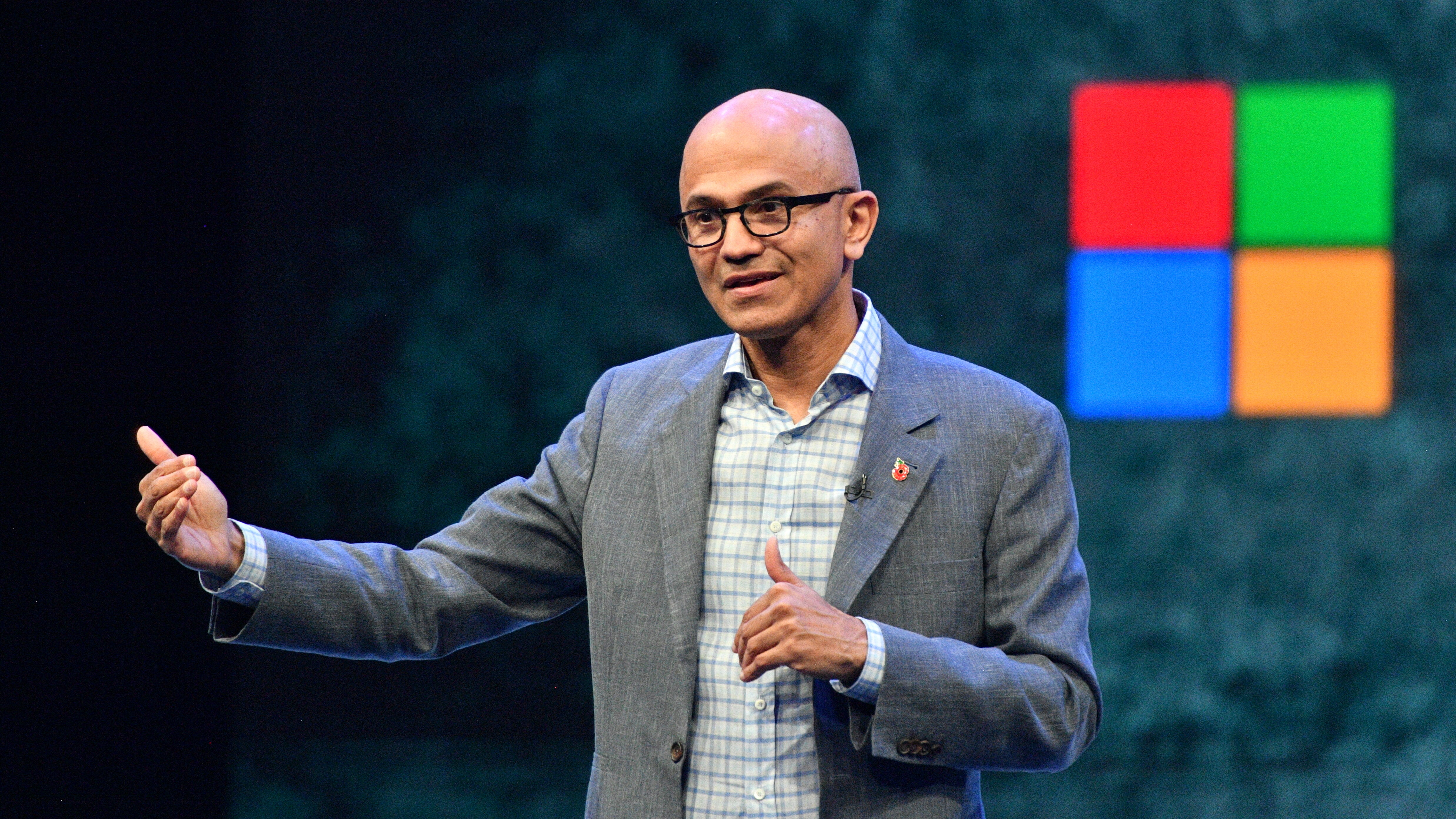 Satya Nadella, CEO da Microsoft, palestrando em evento de tecnologia, com logotipo da Microsoft ao fundo