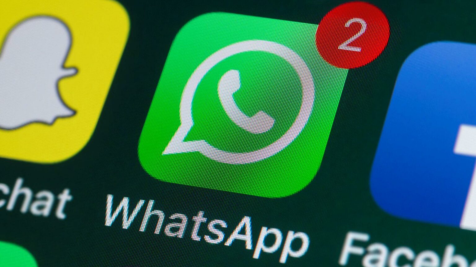 Ícone do aplicativo WhatsApp na tela de um celular, com distintivo vermelho de duas notificações, ao lado dos ícones de Snapchat e Facebook