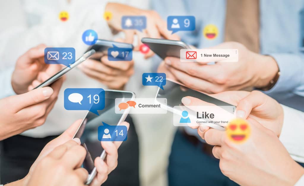 Vídeos curtos estão prejudicando o desenvolvimento cognitivo das crianças, apontam estudos 1 Pessoas segurando smartphones com balões de notificações azuis de mensagens, comentários e curtidas flutuando acima dos aparelhos