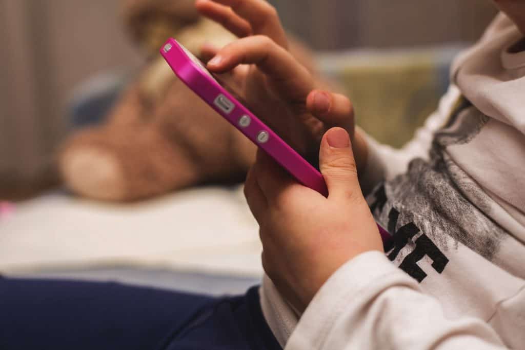 Usuários jovens no Instagram: Zuckerberg revela que muitos mentem a idade 1 Mãos de criança segurando um dispositivo eletrônico magenta com botões laterais, foco no equipamento e fundo desfocado