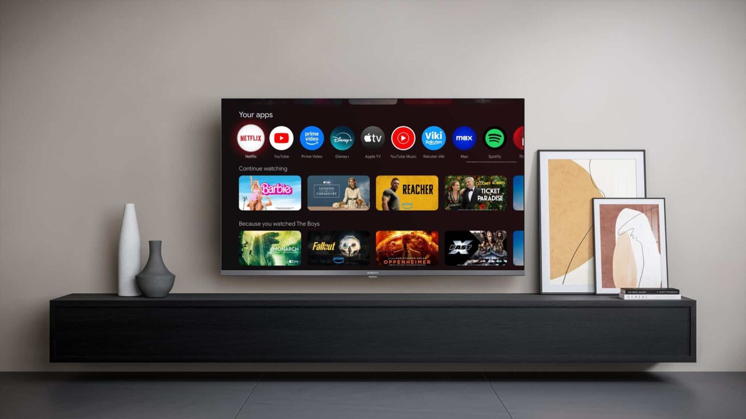Smart TV montada sobre rack escuro em sala clara, exibindo tela inicial com aplicativos como Netflix, YouTube, Prime Video, Disney+, Apple TV e Spotify