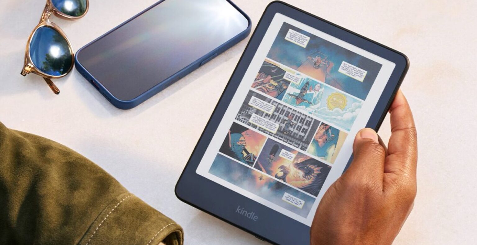 Leitor Kindle azul com tela de tinta eletrônica exibindo página de quadrinhos colorida, segurado por uma mão ao lado de óculos de sol e celular