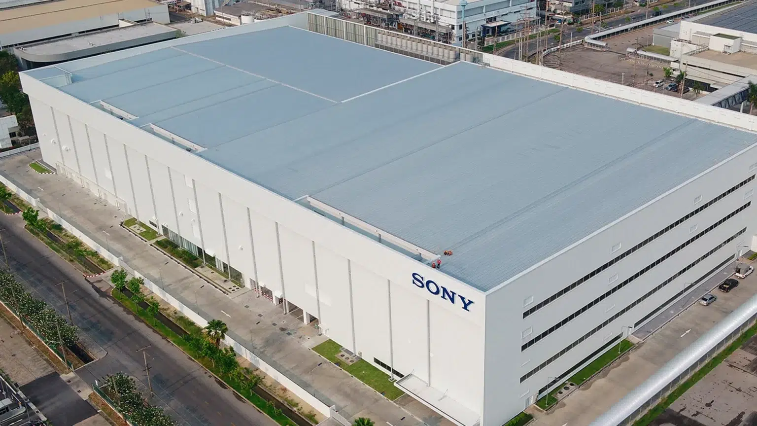 Vista aérea de um grande prédio branco com telhado azul-claro e o nome Sony em azul na fachada, em área industrial com vias e vegetação ao redor