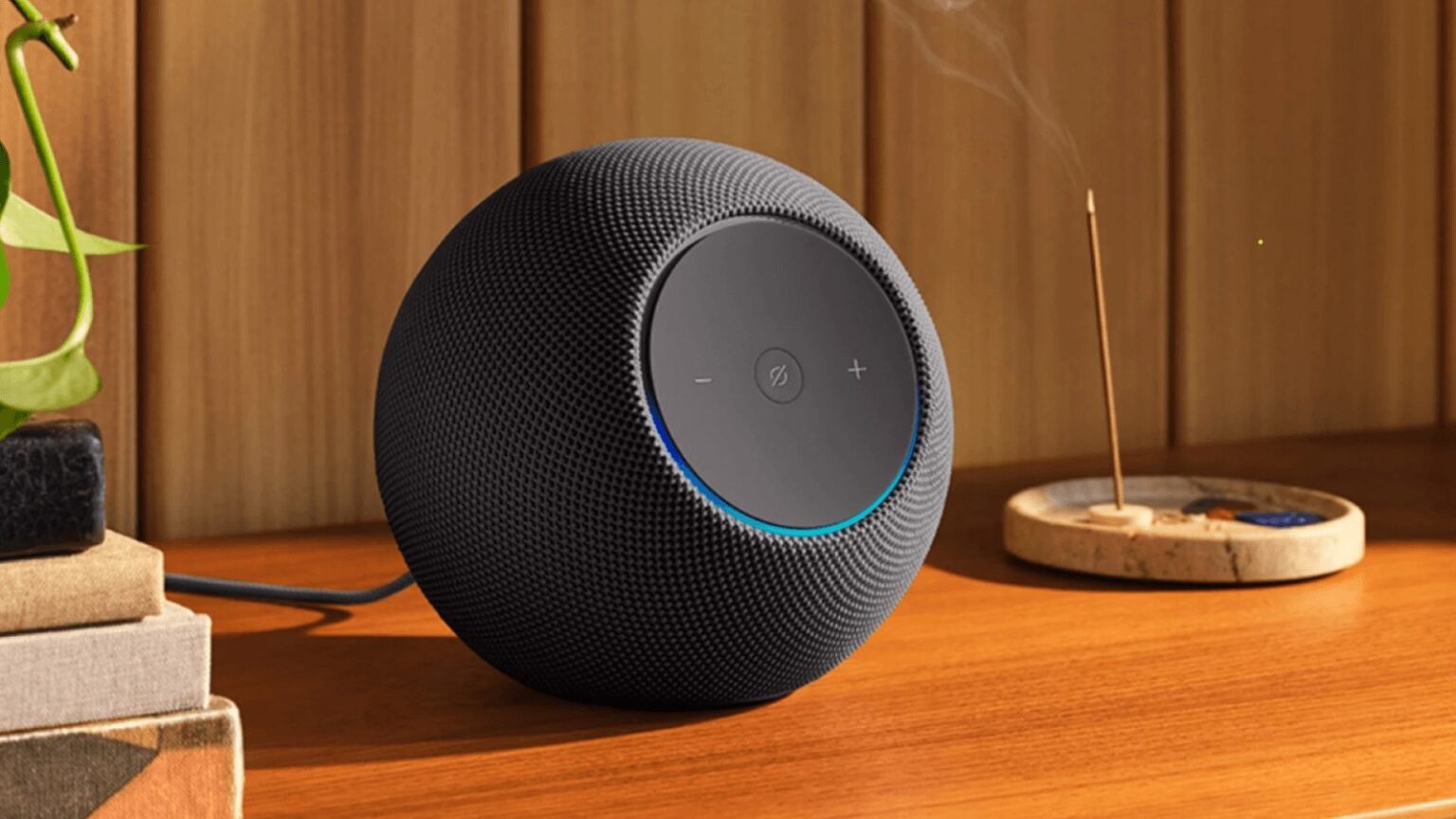 Alto-falante inteligente Echo Dot Max cinza-grafite sobre mesa de madeira, com botões de volume e anel de luz azul, ao lado de um incensário