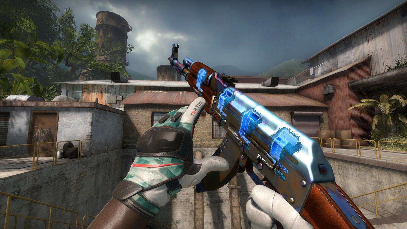 Captura de tela do Counter-Strike 2 mostrando um jogador empunhando um rifle AK-47 com pintura azul e laranja, em um cenário tropical com construções de concre…