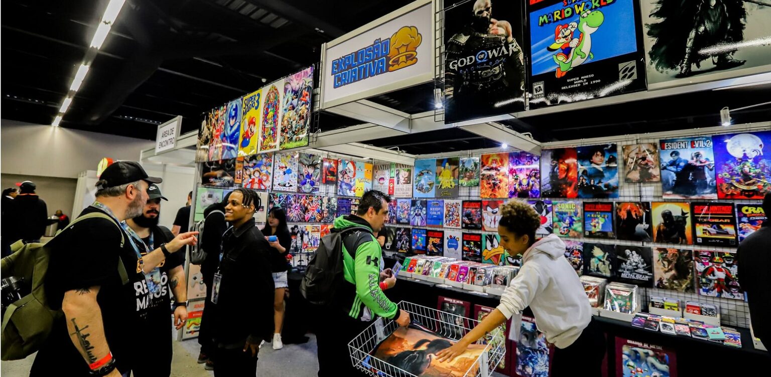 Visitantes em um estande de jogos retrô em evento, com cartazes de Mario, God of War e Mortal Kombat e caixas de jogos expostas em prateleiras e cestas