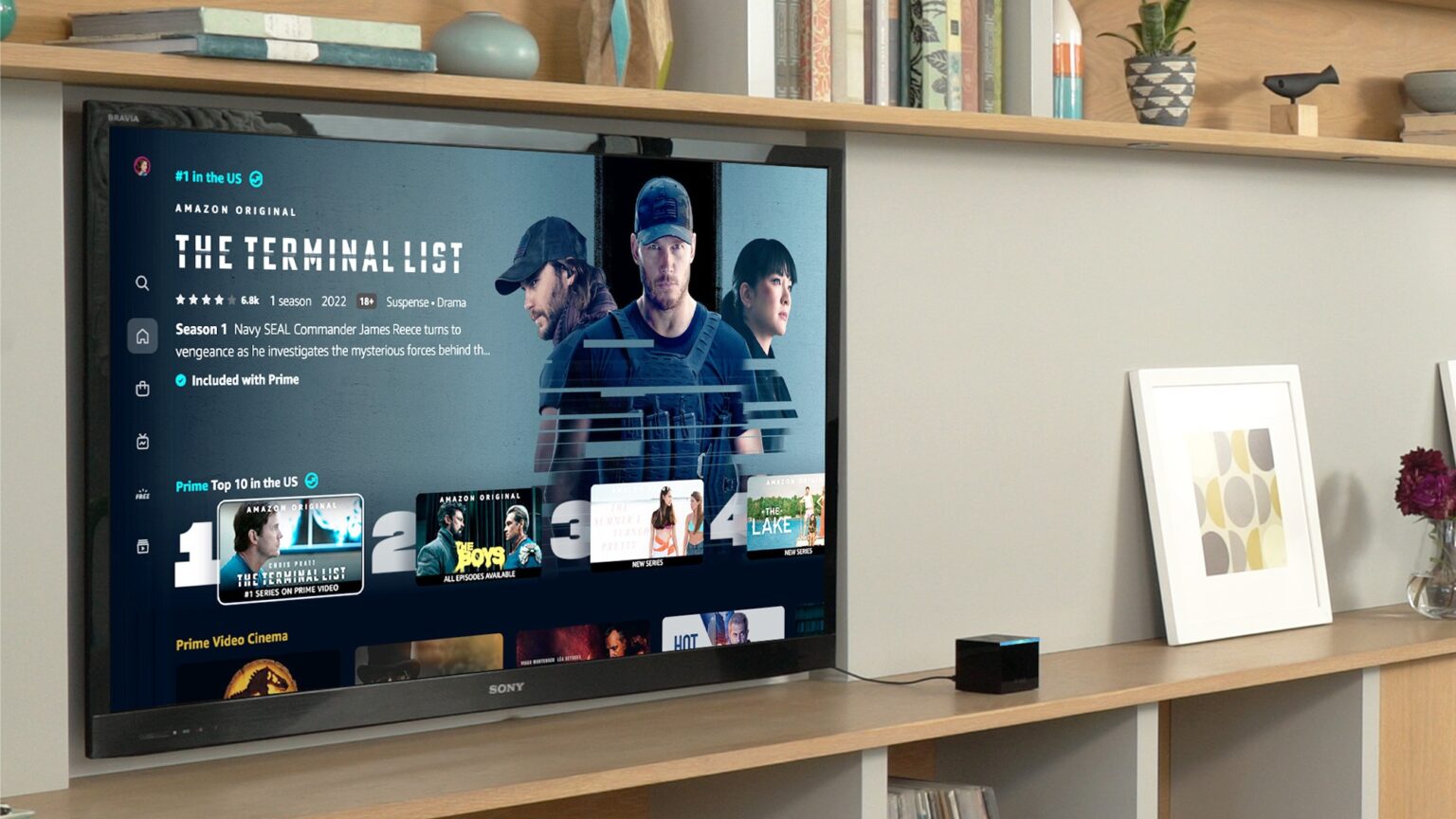 Televisão Sony exibindo a interface do Prime Video com o destaque da série The Terminal List, ao lado de um Fire TV Stick preto sobre estante de madeira