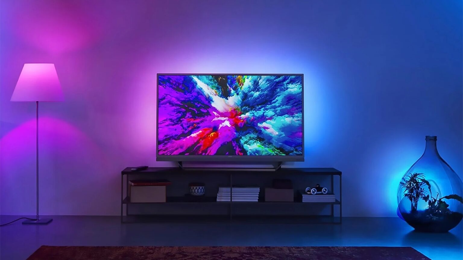 Smart TV Philips com iluminação Ambilight na parede azul e roxa de uma sala, exibindo imagem colorida e abstrata na tela